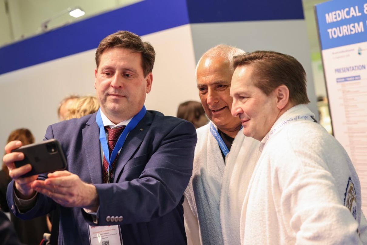 Three men smiling as they look into the front camera of a mobile phone that one of them is holding up. 