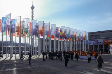 Auf dem Bild sieht man das Außengelände der Messe, zahlreiche Fahnen wehen, im Hintergrund ist der Funkturm zu erkennen