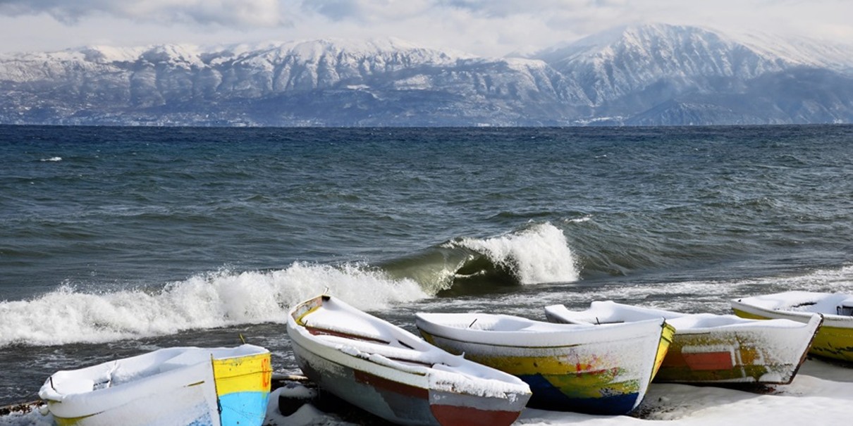 Fishing boats on the water in the foreground, snow-covered mountains at the back of the picture, with a lake in between