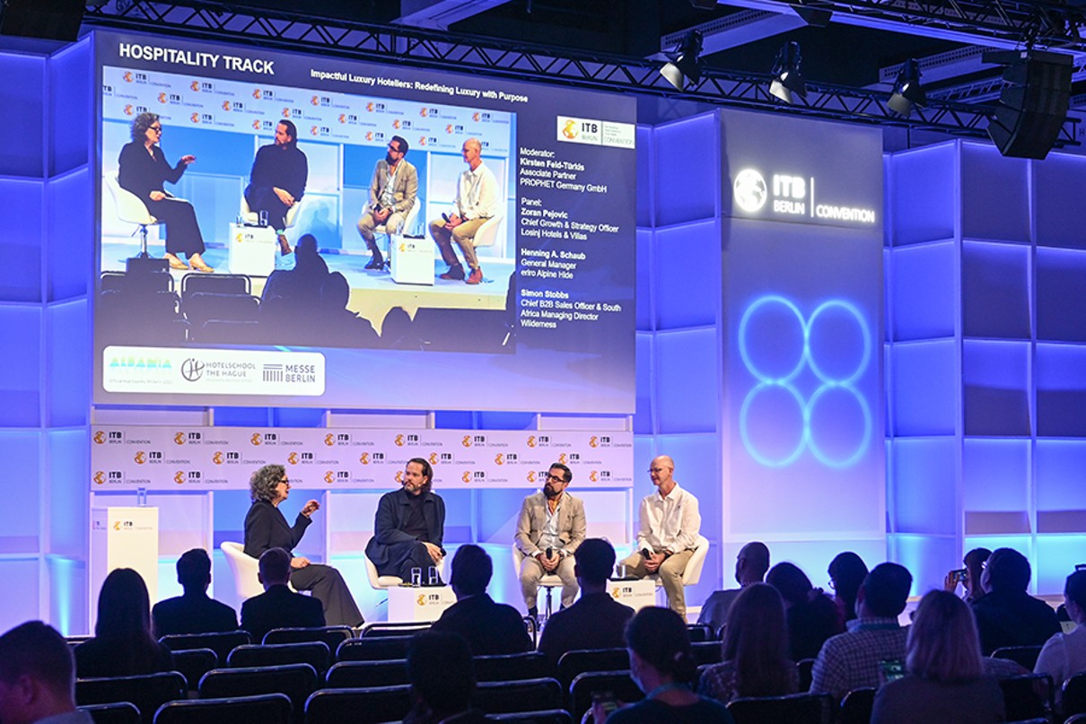 Four people are sitting on stage discussing, with the audience visible in the foreground.