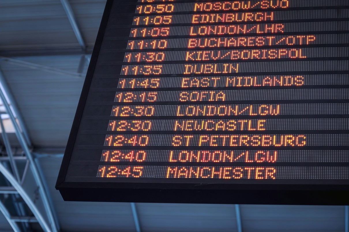 A large, digital flight schedule display board in close-up with the times and names of European cities. 