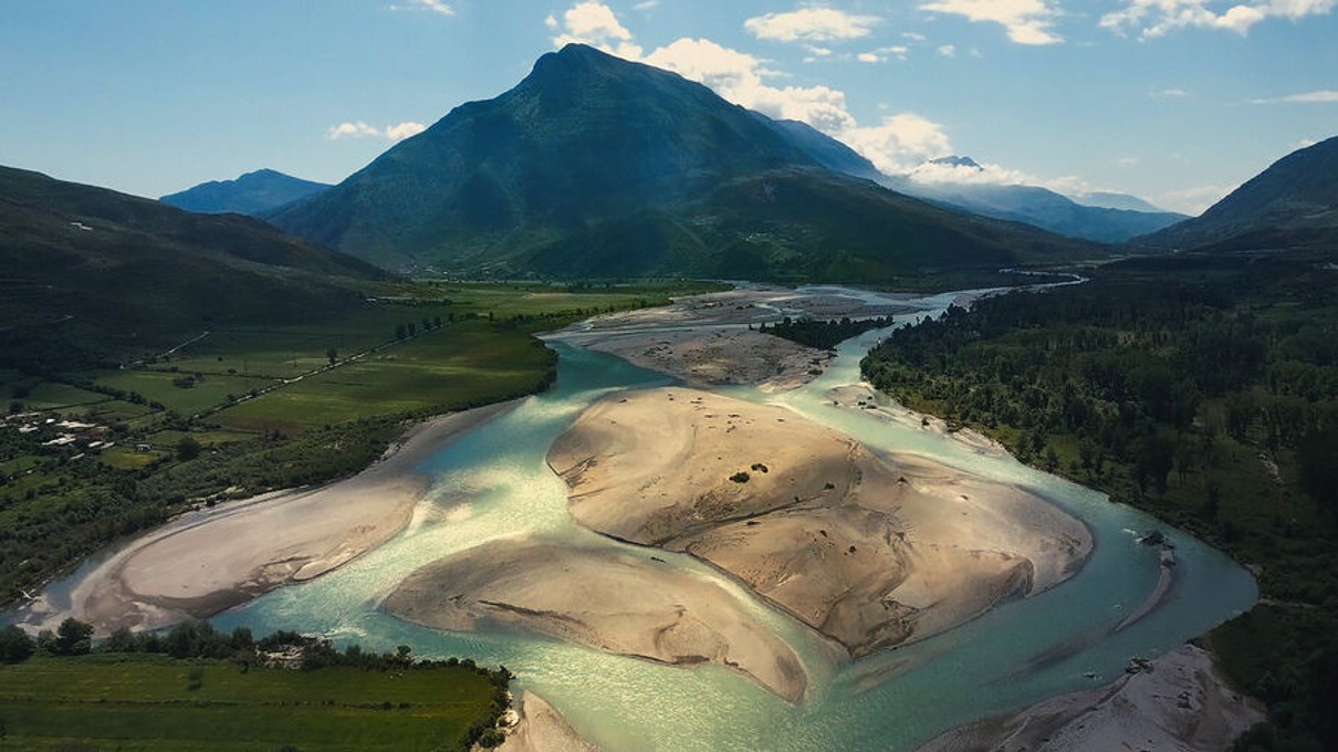 Vjosa River delta, with a mountain landscape and green fields in the background. 