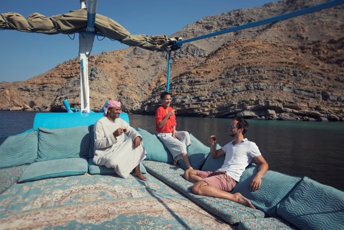 Drei Personen auf einem Boot, umgeben von Wasser und Bergen.