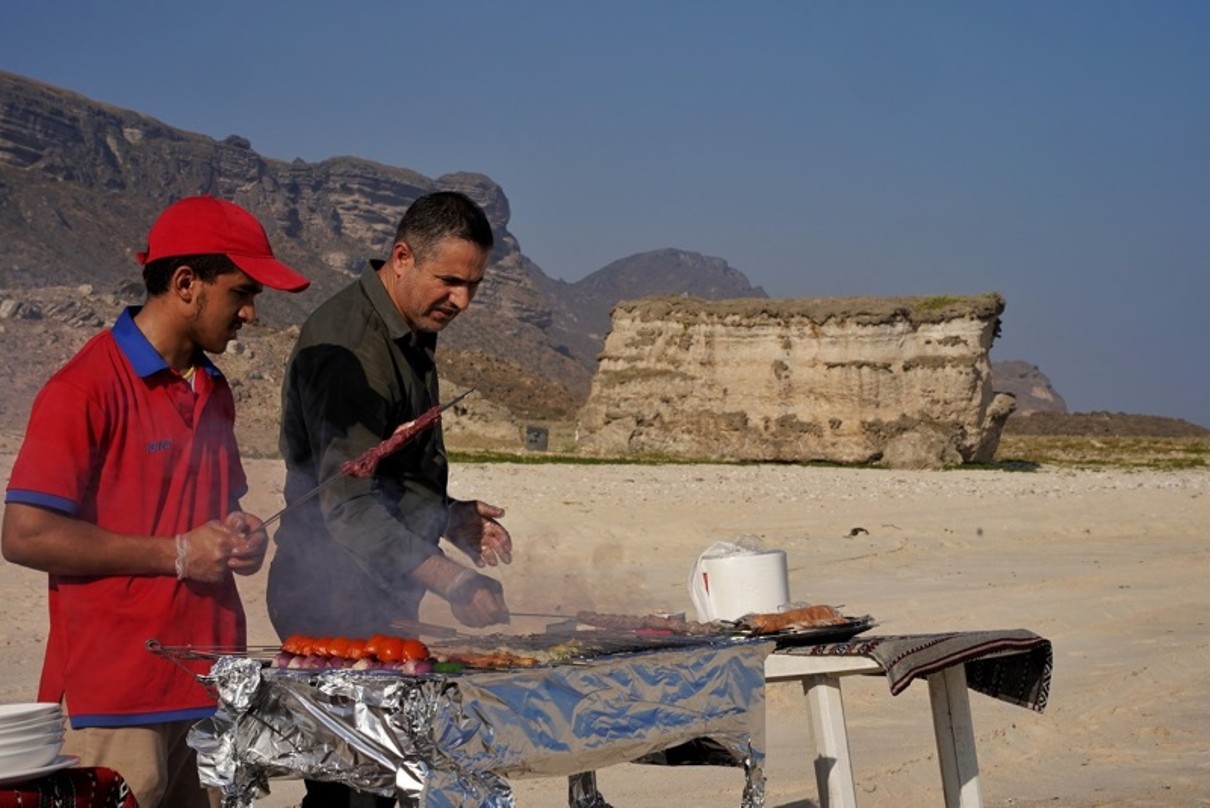Two men at a barbecue, barren mountain landscape in the background