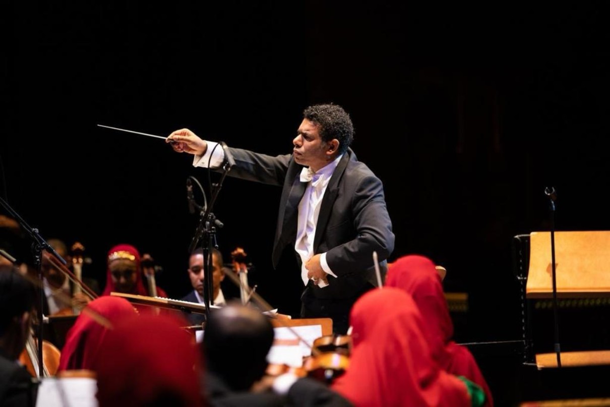 The conductor Hamdan Al Shuaili in focus during a performance, the orchestra musicians are blurred