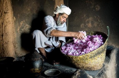 A man sitting on the floor grabbing rose petals from a basket. 