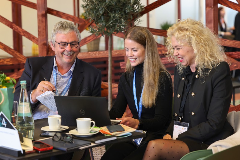 Three people, a man and two women, smiling and looking at the screen of a laptop. 